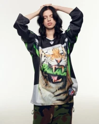Lily McMenamy posing in an oversized graphic tiger jersey and camouflage trousers against a studio background for PALACE Winter 25.