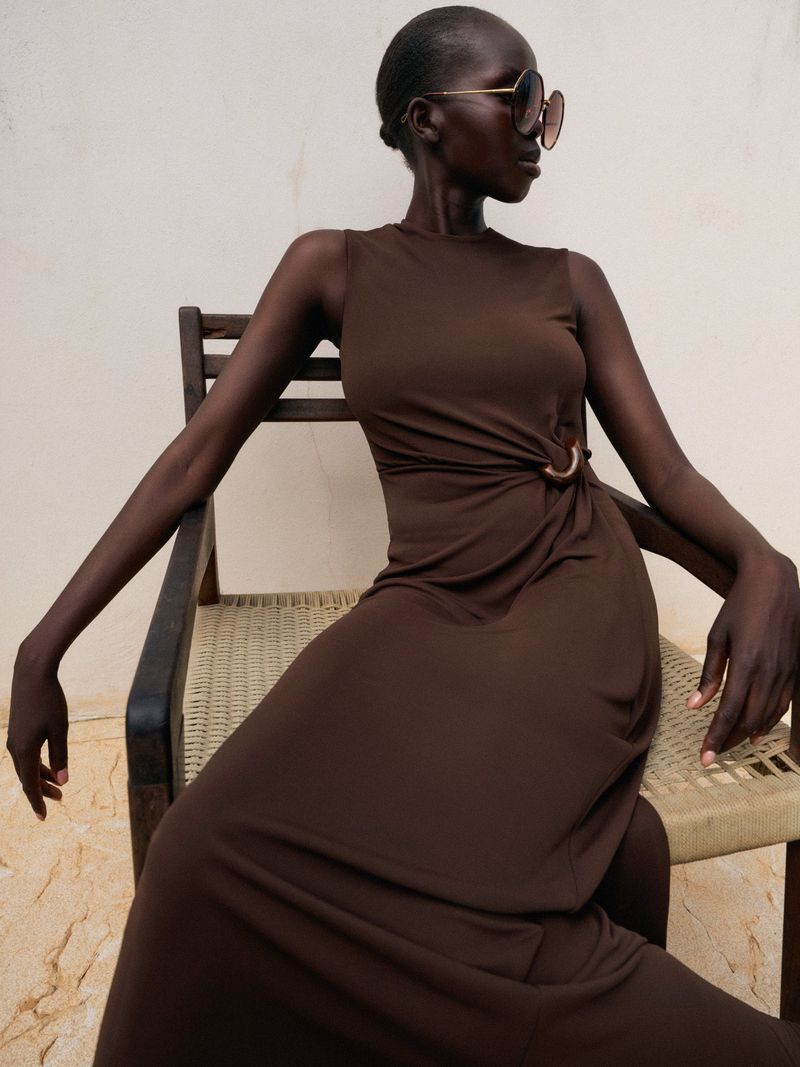 Model Ajok Madel wearing a brown dress seated in a wooden chair for ME+EM May Lookbook.