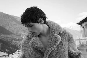 Santiago Rivata wearing an oversized shearling fleece coat in a black and white portrait overlooking alpine mountains.