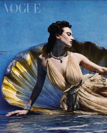 Vogue cover featuring a female model in a gown and jewelry reclining inside a giant clam shell against a blue water backdrop.