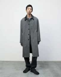 Model Zhuo Chen wearing a long grey tweed coat with a black collar and dark trousers against a minimal studio background.