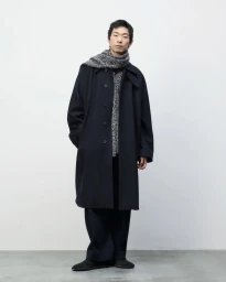 Model Zhuo Chen stands in a white studio wearing an oversized dark navy coat, wide-leg trousers, and a textured grey wool scarf.