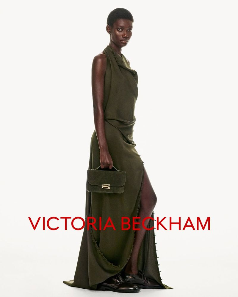 A dark-skinned model poses in a full-length olive dress with a handbag in a studio shot against a white background, highlighting the dress's design.