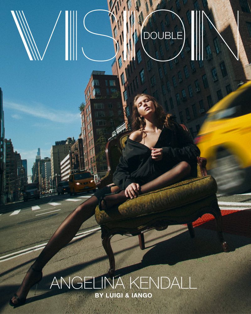 Fashion editorial image of a woman in a black outfit sitting on an ornate chair in the middle of a city street with blurred taxi cabs.