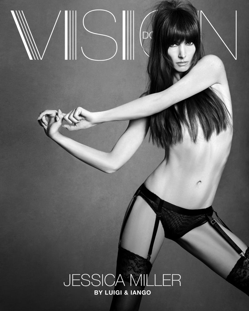 Black and white studio portrait of a slender woman in lingerie and thigh-high stockings, posing in front of a gray backdrop.