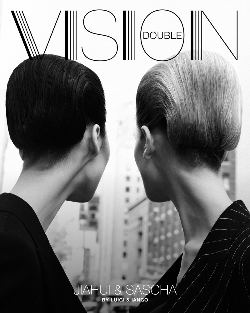 Black and white magazine cover featuring two women with short, slicked-back hair in front of a blurred cityscape.