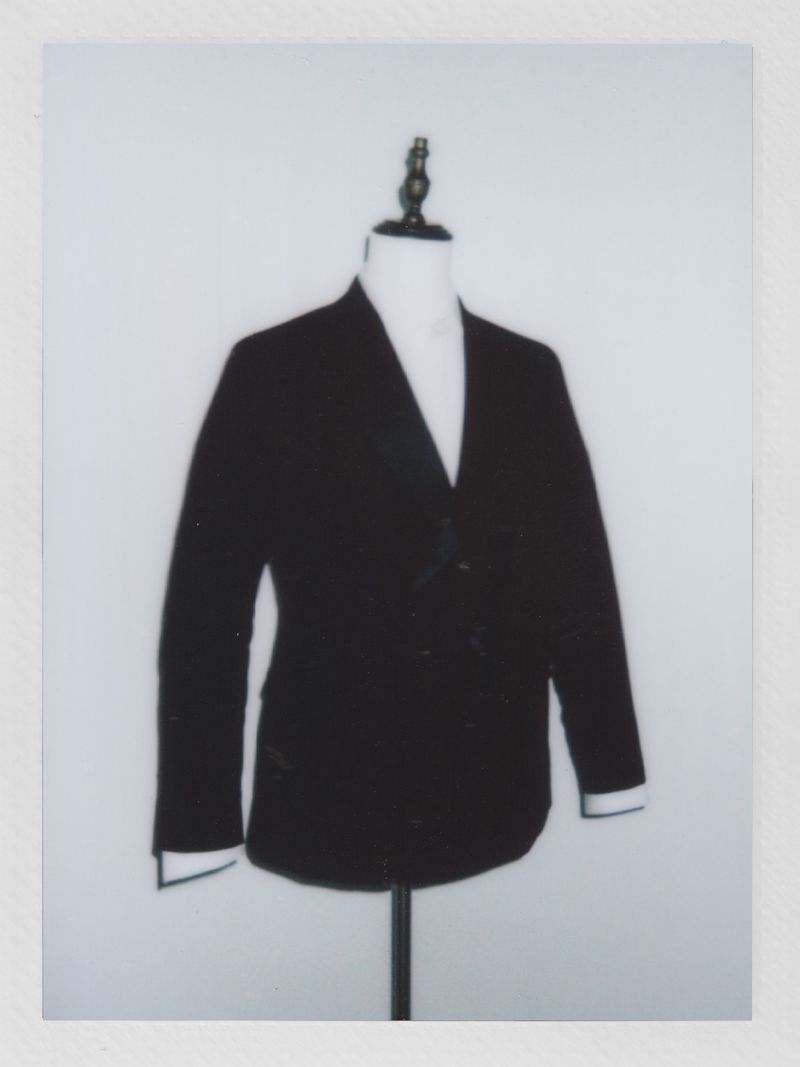 Dark blazer on a mannequin with white shirt, set against a plain white backdrop in a studio setting, fashion or clothing concept.
