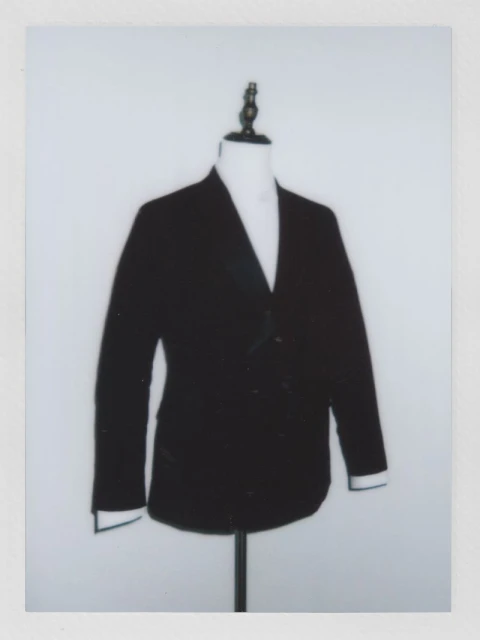 Dark blazer on a mannequin with white shirt, set against a plain white backdrop in a studio setting, fashion or clothing concept.