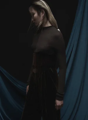 Model Hyunser Park wearing dark top and trousers with a wide belt against a dark background with blue drapery for L'Officiel Italia
