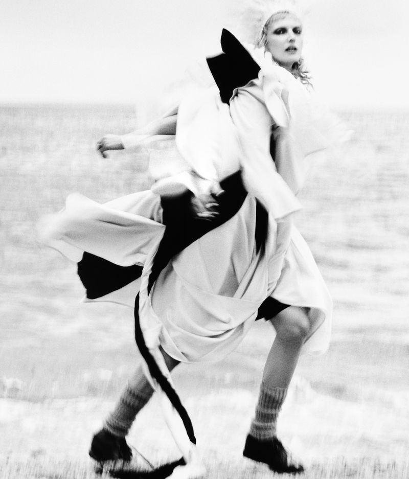 Fashion shot of a woman in a white dress with dark accents, textured socks and dark shoes in an outdoor setting with motion blur.