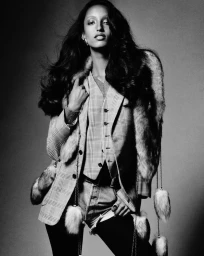 Model Mona Tougaard posing in a plaid blazer, matching vest, fur-trimmed stole, and denim shorts in a black and white studio portrait.