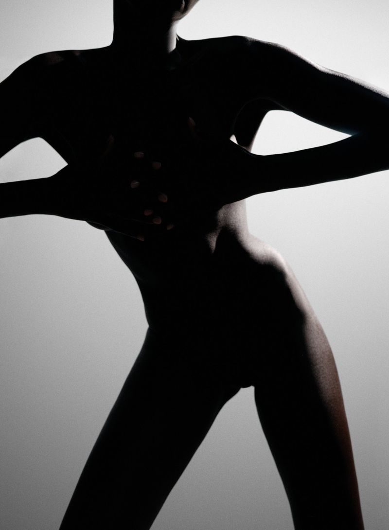 Silhouette of a dark-skinned person posing with hands over the torso against a gradient light gray background in a studio setting.