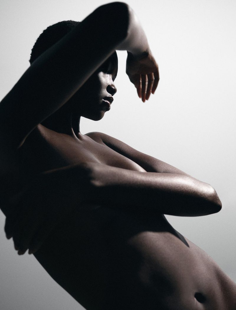 Striking studio portrait of a Black woman with arms raised above her head, capturing a dynamic pose against a neutral background.