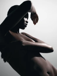 Black female model posing with arms raised and crossed against a neutral studio backdrop with dramatic directional lighting.