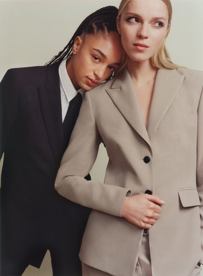 Two women in blazers pose closely together in a fashion-style photo studio, creating a stylish and modern portrait with soft, diffused light.