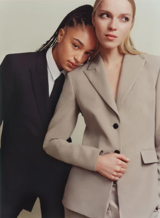 Two women in blazers pose closely together in a fashion-style photo studio, creating a stylish and modern portrait with soft, diffused light.