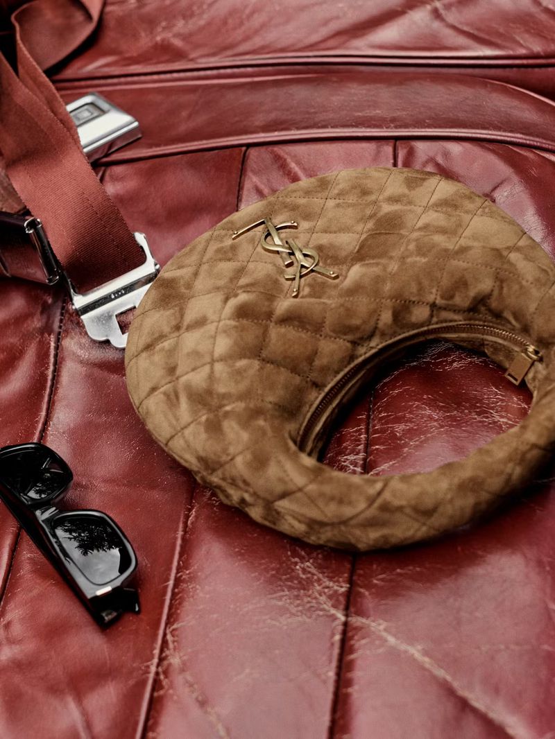 Brown suede YSL purse on a red leather car seat with black sunglasses and a vintage red seatbelt for a luxurious aesthetic.