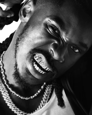 Close-up portrait of an adult man with dreadlocks, wearing a grill and jewelry, looking intensely at the camera in black and white.