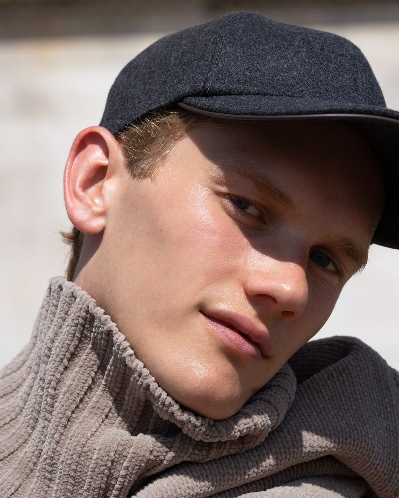 Close-up portrait of an adult male with light skin wearing a gray wool cap and tan corduroy turtleneck sweater, featuring shallow depth of field.