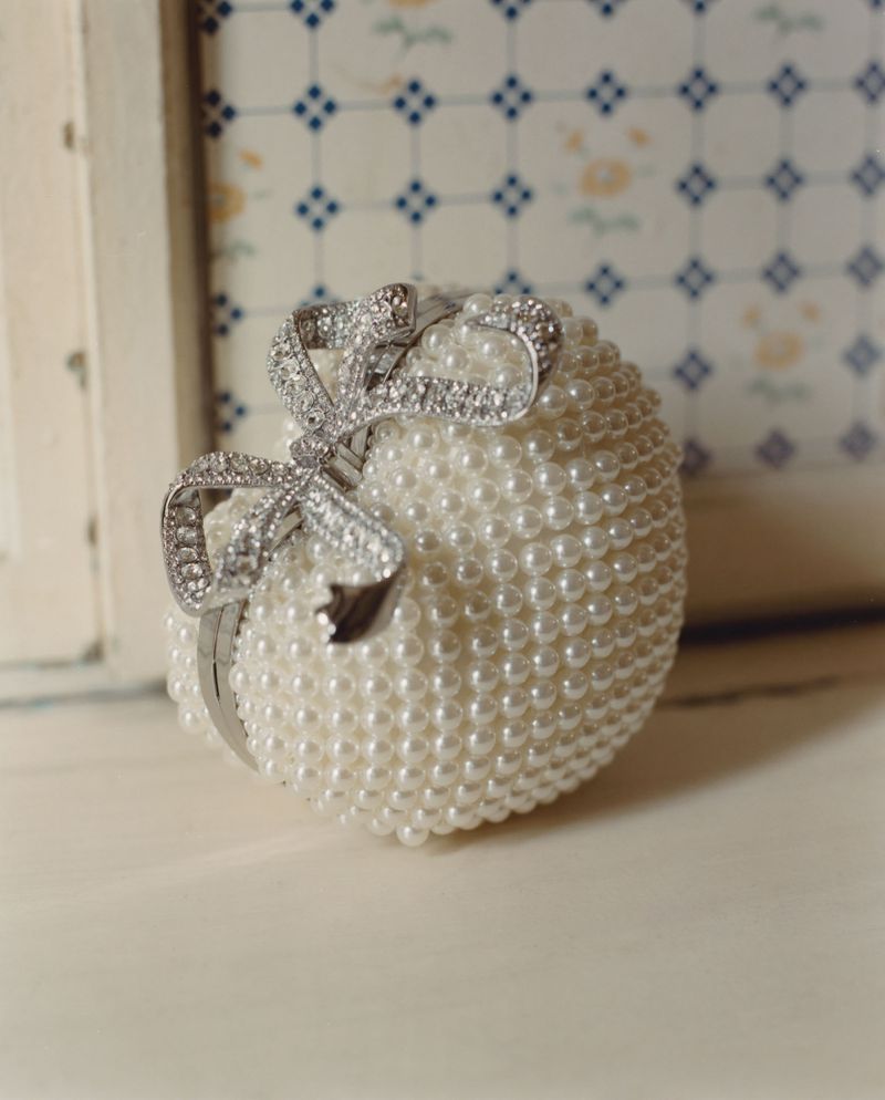 Close-up of an ornate white decorative sphere covered in faux pearls, featuring a detailed silver bow, resting on a light surface.
