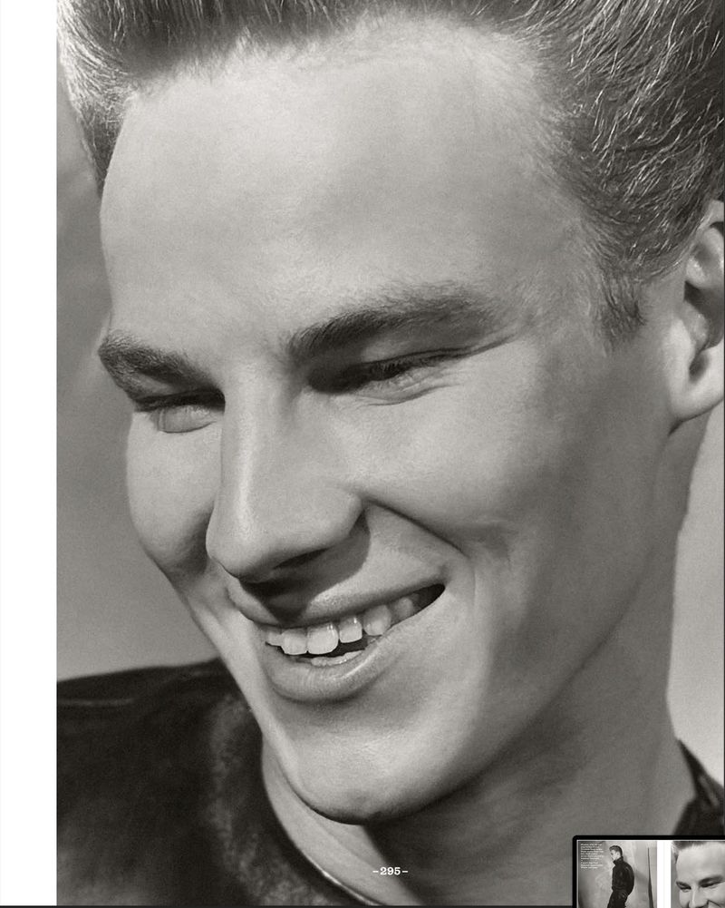 Black and white portrait of a light-skinned adult male with short hair and a wide smile, looking slightly downward in an indoor setting.
