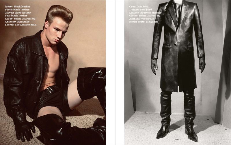 Editorial fashion shot of a male model in a black leather jacket, shorts, gloves and high boots posing indoors on a carpet with neutral wall.
