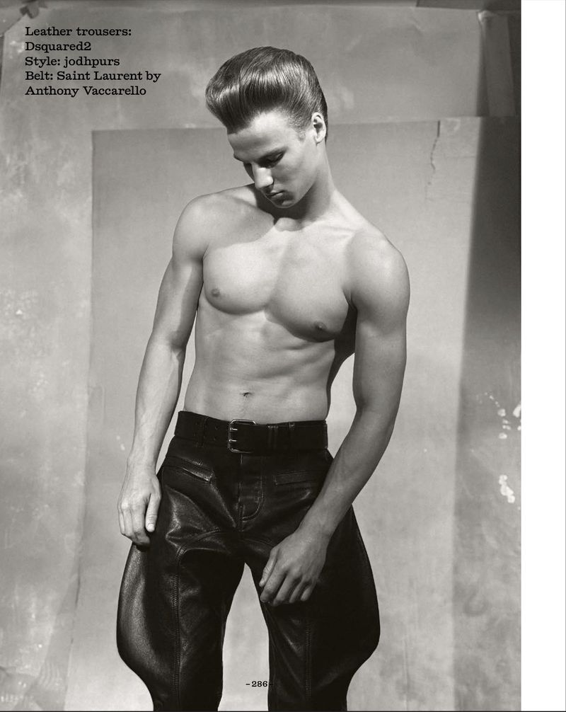 Shirtless male model with pompadour hair wearing black leather jodhpur pants and a buckle belt in a studio setting.