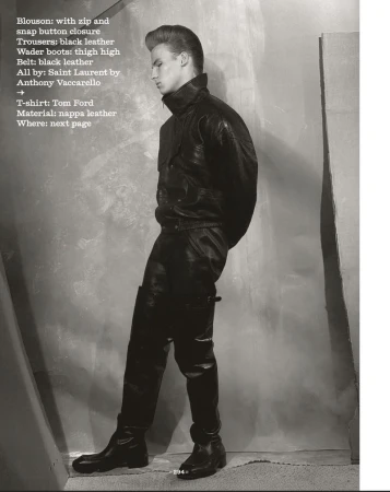 Fashion shoot features a blonde adult male model in a black leather blouson, trousers, and boots, posed in a gray studio setting.