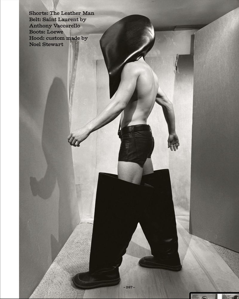 Androgynous fashion shot of a human wearing leather shorts, oversized leather boots and a matching leather hood in a photo studio.