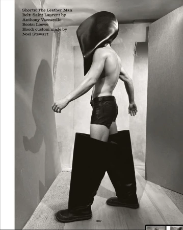 Androgynous fashion shot of a human wearing leather shorts, oversized leather boots and a matching leather hood in a photo studio.