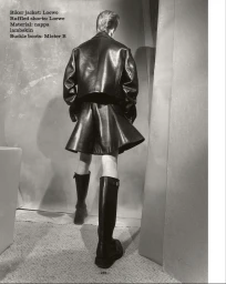 Monochrome fashion editorial featuring a model viewed from behind wearing a dark leather jacket and shorts against a textured backdrop