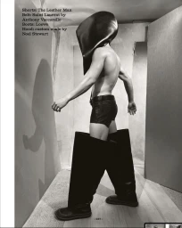 Model wearing a sculptural black leather hood, leather shorts, and exaggerated wide boots in a black and white editorial shoot.