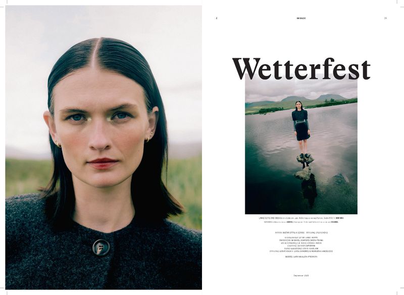 Magazine editorial shot featuring a woman in a grey coat against a green field and a small lake with a standing woman in the background.