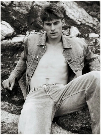 Mikkel Matthiesen in an unbuttoned denim jacket and jeans reclining against coastal rocks in a black and white fashion editorial.