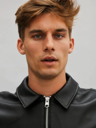 Close-up portrait of model Mikkel Matthiesen wearing a black zip-up leather jacket against a light grey backdrop.