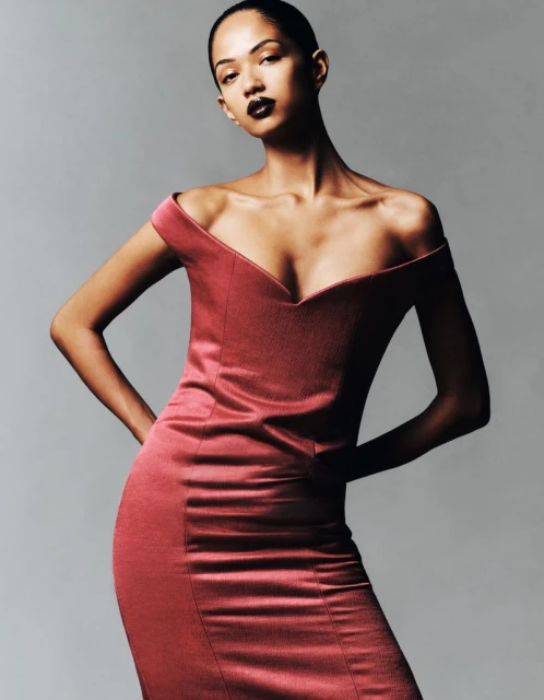 Glamorous portrait of an adult woman posing in a fitted, off-the-shoulder, red dress against a neutral grey studio backdrop.