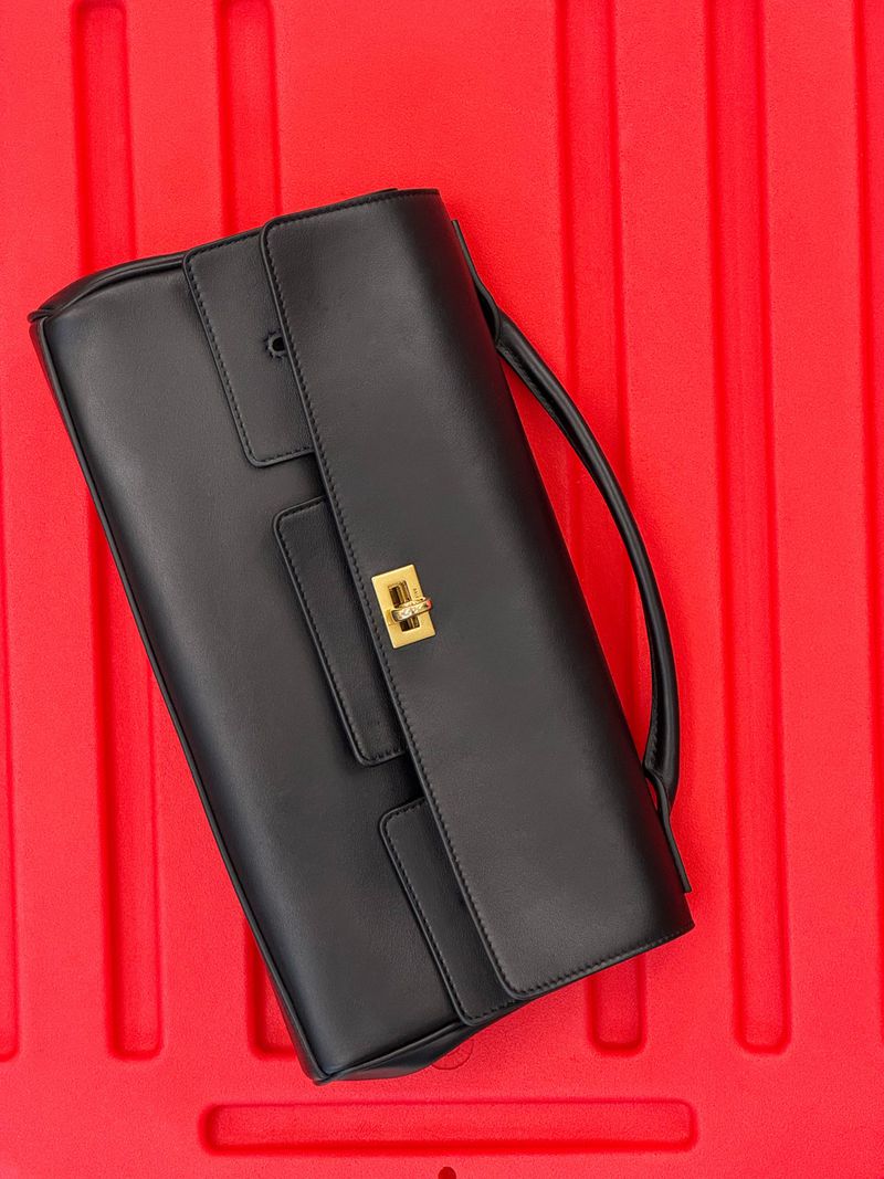 Elegant black leather handbag with golden clasp, lying on a bright red textured surface, emphasizing a sophisticated contrast and high fashion.