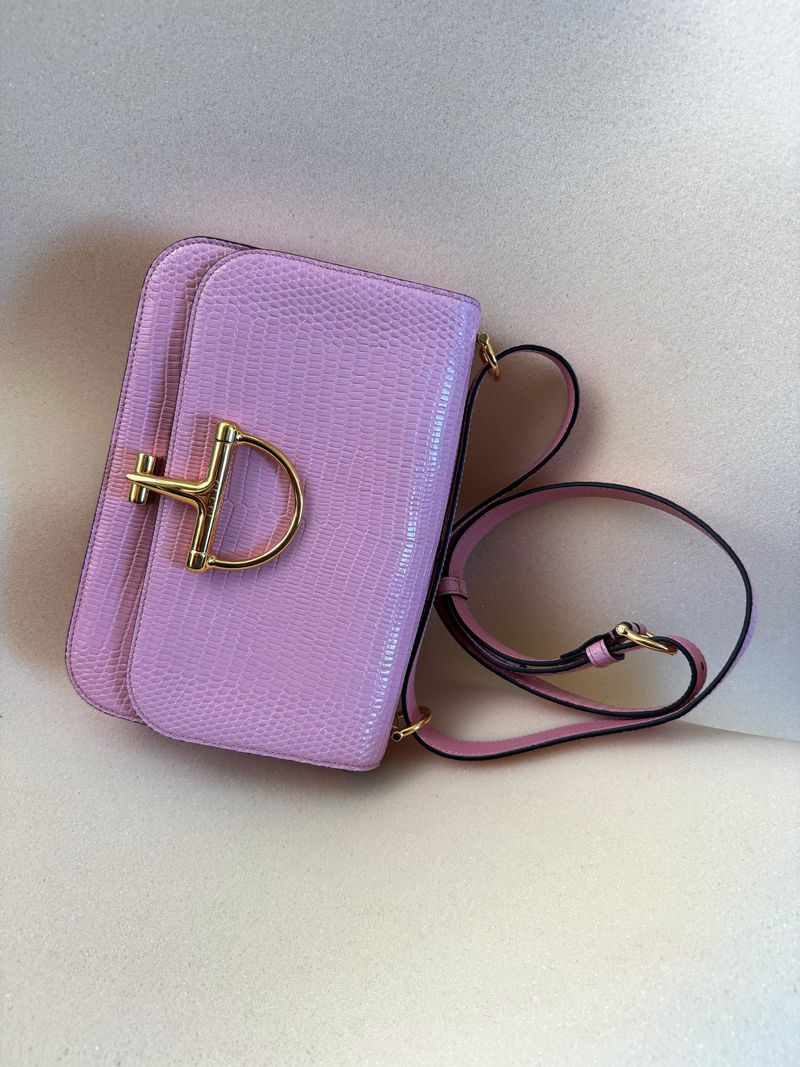 A light purple shoulder bag with a gold-toned clasp and strap on a beige surface, showcasing fashion accessory details.