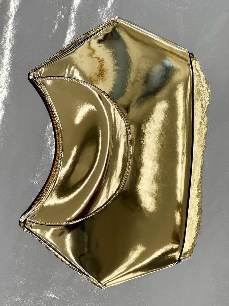 Geometric gold handbag with metallic sheen. Fashionable accessory for special occasions. Modern design against neutral grey backdrop.