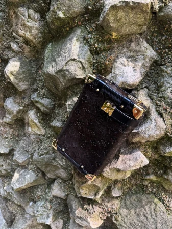 Elevated shot of a small, black Louis Vuitton trunk with gold accents, set against a textured, light-grey rock background.