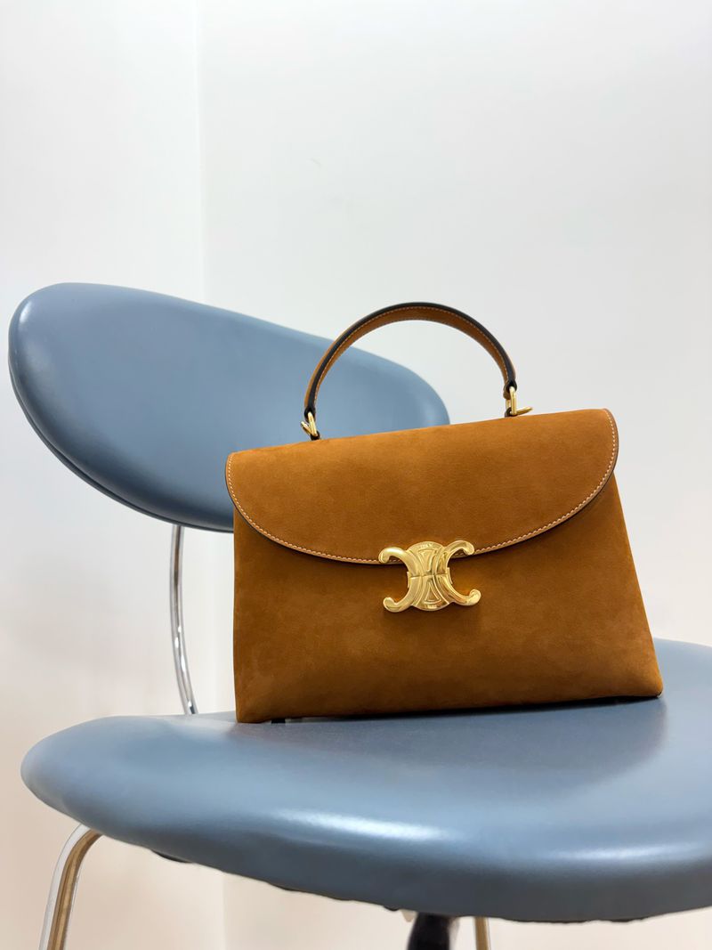 Elevated view of a brown suede top-handle handbag with a gold logo clasp, placed on a blue vintage metal chair against a white wall.