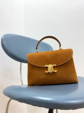 Elevated view of a brown suede top-handle handbag with a gold logo clasp, placed on a blue vintage metal chair against a white wall.