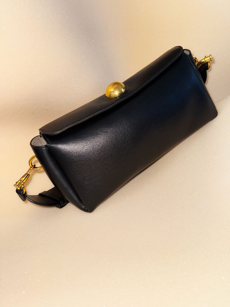 Black leather clutch handbag with gold hardware detail against a beige background. Fashionable accessory with a sleek design.