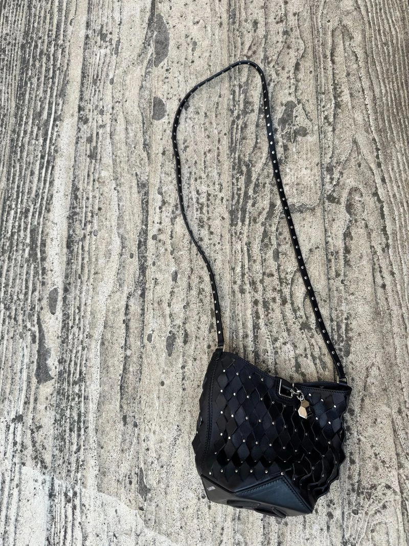 Black woven leather bucket bag with silver studs and a long strap resting on a textured grey concrete surface.
