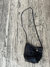 Black woven leather bucket bag with silver studs and a long strap resting on a textured grey concrete surface.