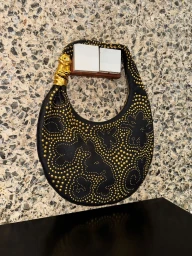 Black hobo handbag with gold stud embellishments hanging against a textured stone wall