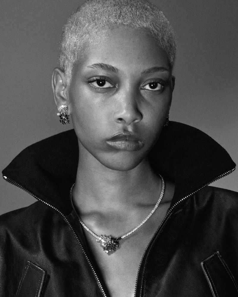 Black and white portrait of an adult female with short white hair wearing a black jacket, earrings, and a necklace with a pendant.