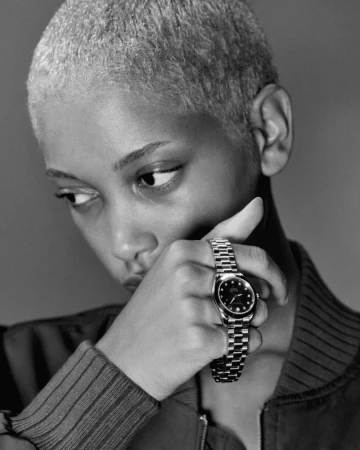 Close-up shot in black and white of a fair-skinned person wearing a watch, hand raised to face in a studio setting.