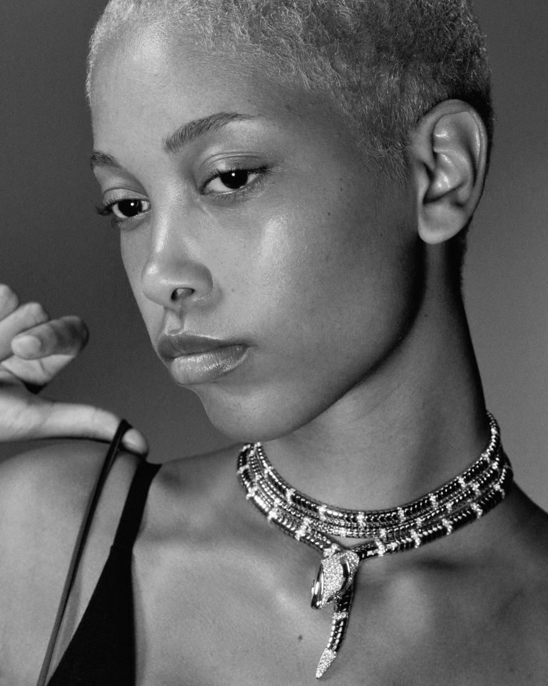 Monochrome portrait of a woman with short blonde hair wearing a snake necklace, against a neutral background in a studio setting.