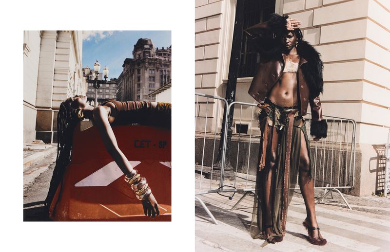 Two women pose in an outdoor fashion editorial, one reclined on a traffic barrier in the city, while the other stands on a crosswalk.